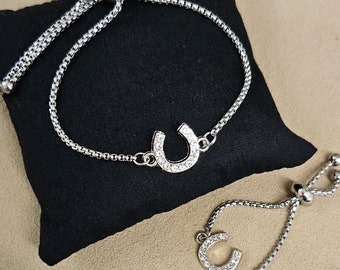May include: Two silver adjustable bracelets with a horseshoe charm set with clear rhinestones. The bracelets are on a black velvet background.