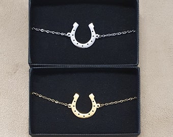 May include: Two horseshoe charm bracelets in black velvet boxes. The top bracelet has a silver horseshoe charm, and the bottom bracelet has a gold horseshoe charm.