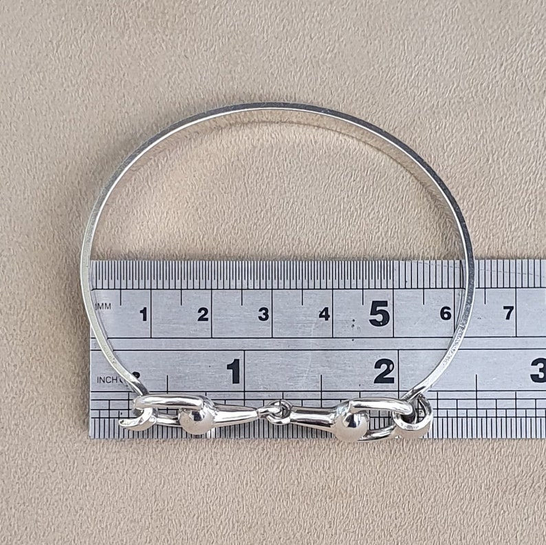 K&ouml;nnte beinhalten: Silbernes Armreif-Armband mit einem Pferdebiss-Design. Das Armband hat einen Durchmesser von 12,7 cm.