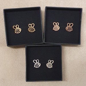 May include: Three black boxes containing gold and silver bee-shaped earrings. The boxes are lined with black velvet.
