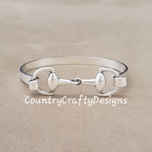 K&ouml;nnte beinhalten: Silbernes Armreif-Armband mit einem Pferdebiss-Design. Das Armband ist offen und hat einen schlichten, eleganten Look.