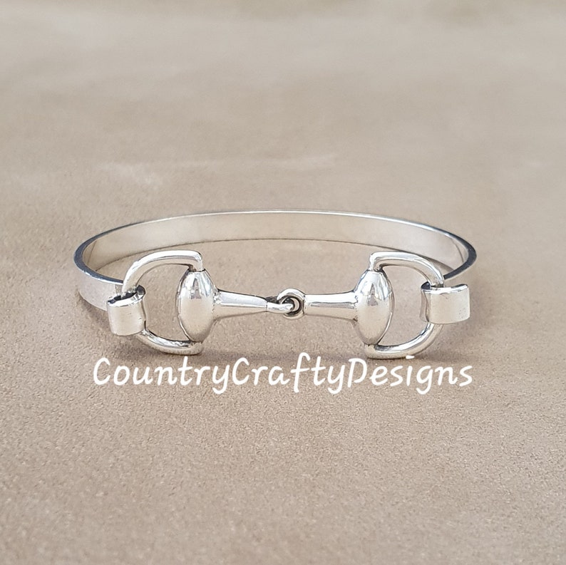 K&ouml;nnte beinhalten: Silbernes Armreif-Armband mit einem Pferdebiss-Design. Das Armband ist offen und hat einen schlichten, eleganten Look.