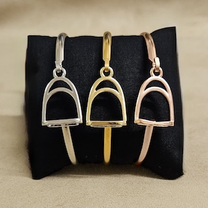 May include: Three gold-toned bracelets with a horse bit charm. The bracelets are displayed on a black background.