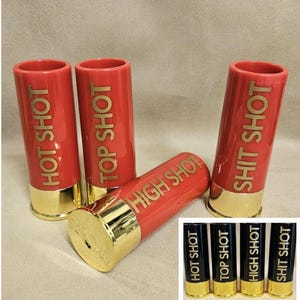 Könnte beinhalten: Vier rote Schnapsgläser mit goldenen Rändern und den aufgedruckten Wörtern "Hot Shot", "Top Shot", "High Shot" und "Shit Shot". Vier schwarze Schnapsgläser mit goldenen Rändern und den gleichen Wörtern darauf.