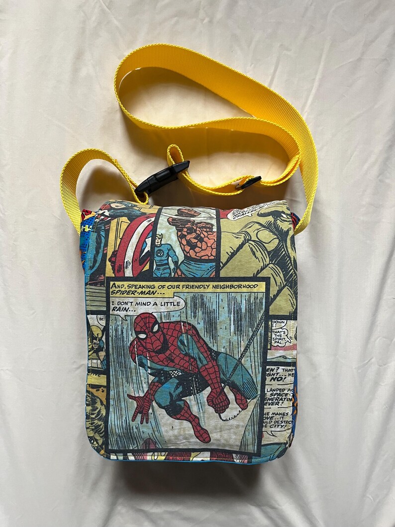 May include: A rectangular comic book-themed crossbody bag with a yellow strap. The bag features panels with Spider-Man and other Marvel characters. The text "AND, SPEAKING OF OUR FRIENDLY NEIGHBORHOOD SPIDER-MAN... I DON'T MIND A LITTLE RAIN..." is visible.