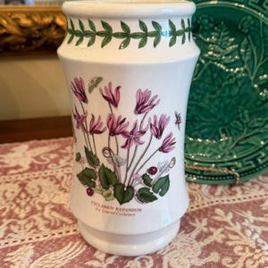 May include: White ceramic vase with a botanical design featuring pink cyclamen flowers and green leaves. The vase has a green leaf border and the text "CYCLAMEN REPANDUM by Linnead Cyclamen".