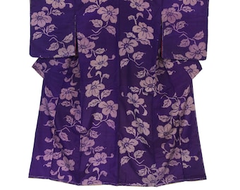 May include: A purple kimono with a floral pattern. The kimono features a repeating design of light purple flowers and green leaves against a dark purple background. The garment is laid flat, showcasing its full shape and design.
