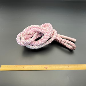 May include: A pink and white braided rope with a textured surface.