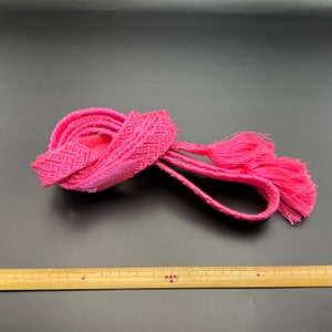 May include: A pink braided cord with tassels. The cord is approximately 120 cm long.
