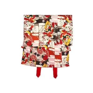 Puede incluir: Un kimono con estampado rojo, blanco y negro con un diseño floral. El kimono tiene una silueta larga y fluida y está atado con una faja roja.