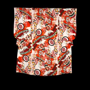Puede incluir: Un kimono japonés tradicional con un vibrante estampado floral. El kimono presenta un fondo blanco con un diseño repetido de elementos rojos, naranjas y negros, incluyendo flores estilizadas y formas geométricas. Las mangas son anchas y la prenda está doblada.