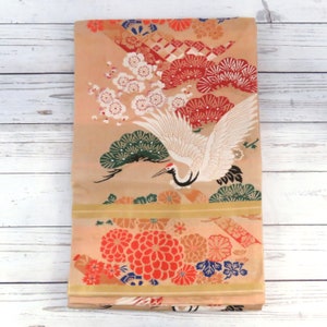 May include: A beige silk fabric with a traditional Japanese design. The fabric features a white crane with red, green, and black accents. The bottom half of the fabric features a floral pattern with red, orange, and blue flowers.