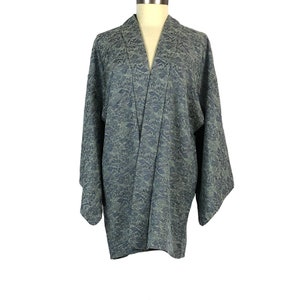 May include: A blue and gray patterned kimono-style jacket with wide sleeves. The jacket is displayed on a mannequin against a white background. The fabric has a subtle, textured design.