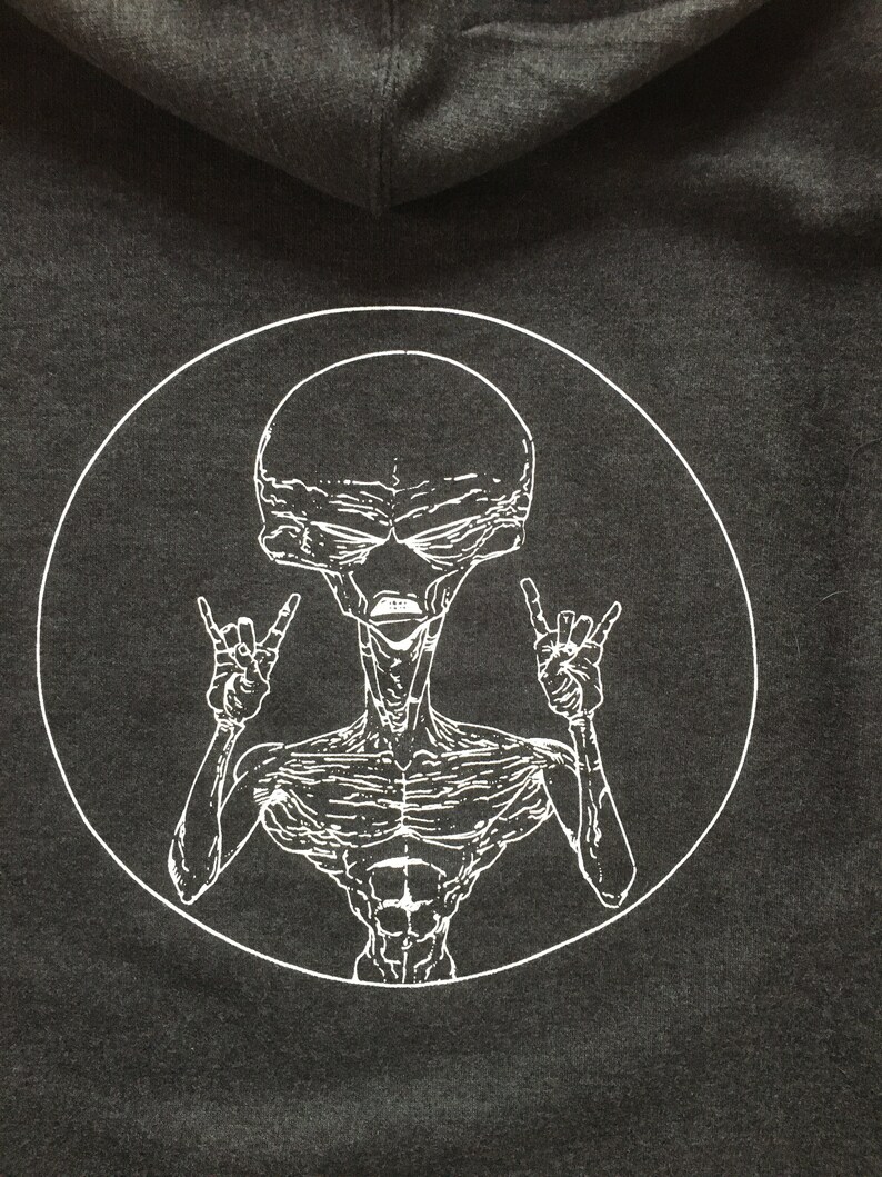 May include: A black hoodie with a white circle graphic of an alien with a large head and a muscular body. The alien is making the rock and roll hand gesture with both hands.