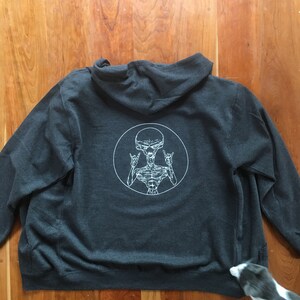May include: A dark gray hooded sweatshirt with a white graphic of an alien with its arms raised in a rock and roll hand gesture. The alien is inside a white circle.