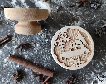 May include: A wooden Christmas cookie cutter with a design of a car carrying a Christmas tree. The cutter is on a gray surface with flour and star anise.