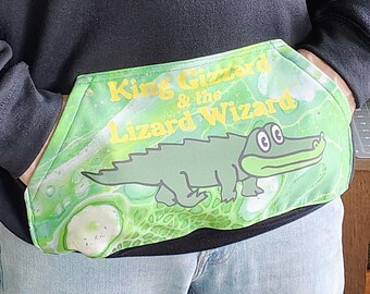 May include: Black hoodie with a large front pocket featuring a green and white design. The pocket has a cartoon alligator and the text "King Gizzard & the Lizard Wizard" in yellow. The person is wearing light blue jeans.