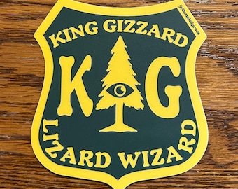 May include: A shield-shaped sticker with a dark green background and yellow border. The text "KING GIZZARD LIZARD WIZARD" is in yellow, along with the letters "K" and "G" and a tree with an eye in the center.