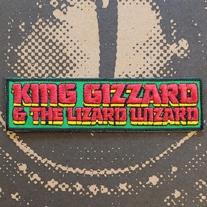 Könnte beinhalten: Ein rechteckiger gestickter Aufnäher mit dem Text KING GIZZARD & THE LIZARD WIZARD in roten Buchstaben mit gelben Umrandungen. Der Text befindet sich auf einem hellgrünen Hintergrund und der Aufnäher hat einen dünnen, schwarz gestickten Rand.