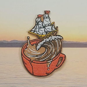 Puede incluir: Un parche bordado que representa una taza de café roja con un líquido marrón y un velero blanco navegando en una ola marrón. El parche mide aproximadamente 5 cm de ancho.