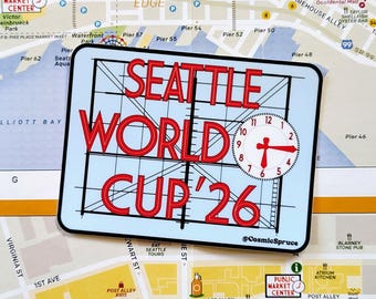 May include: A rectangular sticker featuring the red text SEATTLE WORLD CUP '26 layered over a black grid and a white clock face showing the time. The sticker includes the small text @CosmicSpruce in the bottom right corner and is placed on a map.