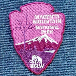 Könnte beinhalten: Ein magenta- und lila-farbener, gestickter Aufnäher mit dem Text "Magenta Mountain National Park". Der Aufnäher zeigt eine Bergkette, einen Baum und eine Elefanten-Silhouette. Der Aufnäher hat die Form eines Pfeilspitzes.