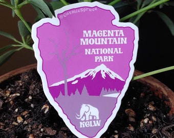 May include: A magenta sticker in an arrowhead shape, featuring the text "Magenta Mountain National Park." The design includes a mountain range, a tree, and an elephant illustration. The sticker also has the text "KGLW" at the bottom and the Instagram handle "@CosmicSpruce" at the top.