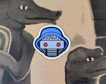 May include: A die-cut sticker featuring a stylized robot head with a blue hood, a grey faceplate, two circular red eyes, and a brain-like texture on top. The small text at the bottom of the sticker reads CosmicSpruce in a simple black font.
