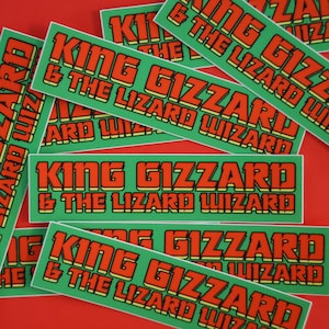 Może przedstawiać: Wiele zielonych i czerwonych naklejek z tekstem "King Gizzard & The Lizard Wizard" w pogrubionym, blokowym kroju pisma.