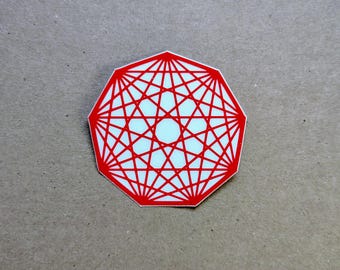 May include: A sticker shaped as a nonagon featuring a white background with a complex, symmetrical geometric pattern of intersecting red lines that form a star-like design radiating from a central white circle within the polygon's perimeter.