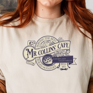 Puede incluir: Una camiseta beige con un logotipo de estilo vintage para "Mr. Collins' Cafe" que presenta un pastel, texto e ilustraciones. El logotipo dice "Serving the Best", "Mr. Collins' Cafe", "Exemplary Vegetables", "Boiled Potatoes" y "Since 1815".