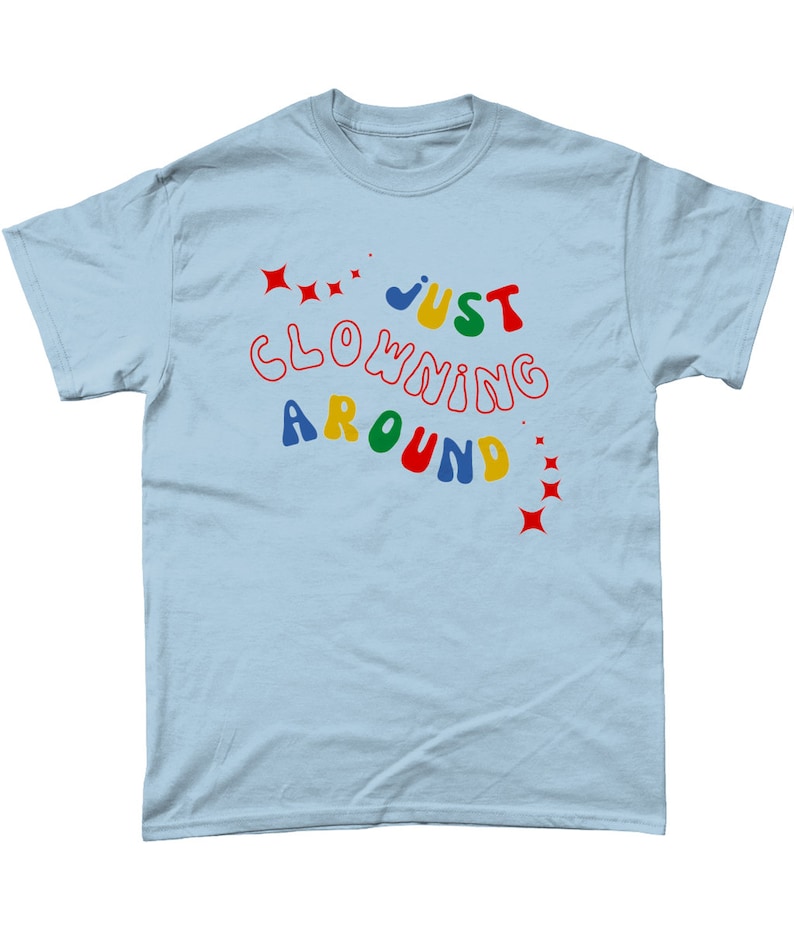 Op de afbeelding: Lichtblauw T-shirt met de tekst "JUST CLOWNING AROUND" in kleurrijke, speelse letters.