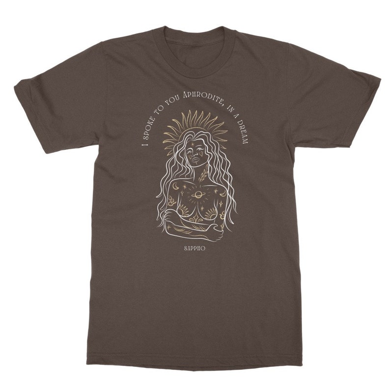 May include: A brown t-shirt with a white line drawing of a woman with a sun halo and celestial tattoos. The text "I spoke to you Aphrodite, in a dream" is written around the woman's head. The text "Sappho" is written below the woman.