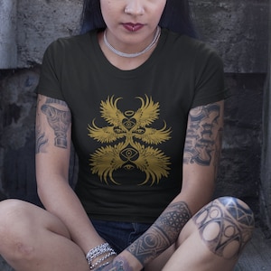 May include: A black t-shirt with a gold graphic of a stylized angel with multiple eyes and wings.