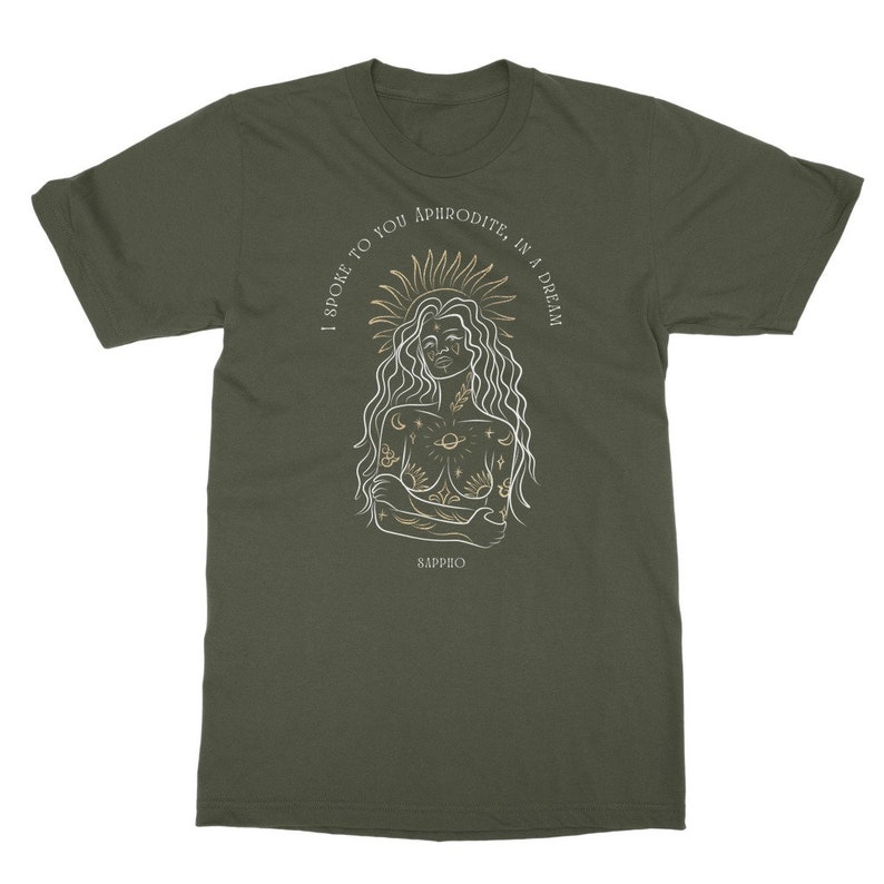 May include: A green t-shirt with a white outline of a woman with a sun halo and celestial tattoos. The text "I spoke to you Aphrodite, in a dream" is written in a gold script around the woman's head. The text "Sappho" is written in gold at the bottom of the shirt.