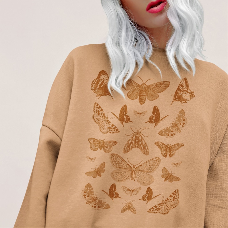 May include: A tan sweatshirt with a print of various brown butterflies and moths. The print is centered on the front of the sweatshirt.