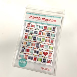 May include: A quilting pattern titled "Thimble Blossoms" by Camille Roskelley. The pattern features a colorful quilt design with spools of thread and a red heart. The pattern is labeled "Spools 2" and is part of the "Sweet Simple" collection.