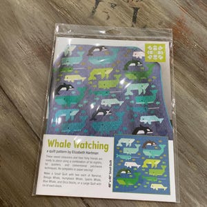 May include: A quilt pattern titled "Whale Watching" by Elizabeth Hartman. The pattern features various whale illustrations in shades of blue, green, and black on a blue background. The quilt measures 48 x 48 inches.