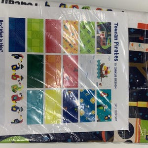 May include: A close-up of a sample pack of fabric featuring a variety of colorful patterns. The fabric is labeled "Toucan Pirates by Zirkus Design" and includes a variety of toucan, pirate, and tropical designs.