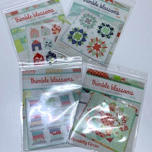 May include: Four mini quilt pattern packets in clear plastic sleeves. The packets feature colorful quilt designs with the text "thimble blossoms" and "by camille roskelley". The patterns include "Swoon #170" and "Piccadilly Circus #189".