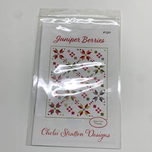 May include: A quilting pattern titled "Juniper Berries" by Chelsi Stratton Designs. The pattern features a red, green, and gray color scheme with a starburst design. The pattern is labeled as "Layer Cake Friendly" and is numbered #150.