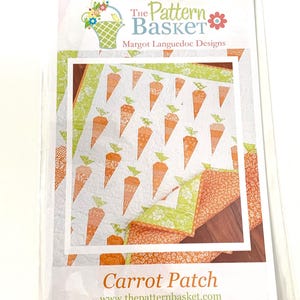 May include: A package for a quilt pattern titled "Carrot Patch" by Margot Languedoc Designs. The pattern features a repeating design of orange carrots with green tops on a white background. The package has a floral basket logo.