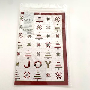 May include: A red and white fabric panel with a Christmas tree pattern. The panel features a variety of trees, stars, and the word "JOY" in large letters. The panel is labeled "Spread Joy" and "PATO39" and is a sewing pattern by BasicGrey.