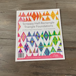 May include: A white paper foundation with colorful geometric designs. The text reads "Scrappy Half-Rectangle Triangle Foundations" and "25 Different Paper-Pieced Designs - 3" x 6" Finished Size". The paper is labeled "100 Scrap-Busting Paper Foundations by Gardunia".