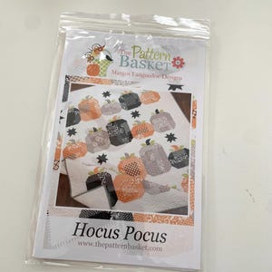 May include: A quilting pattern for a quilt featuring a Halloween theme with pumpkins and stars. The pattern is called "Hocus Pocus" and is from The Pattern Basket by Margot Languedoc Designs.