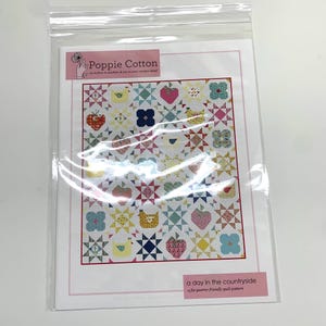 May include: A quilting pattern titled "a day in the countryside" by Poppie Cotton. The pattern features a colorful quilt design with a variety of motifs, including strawberries, chickens, and flowers.