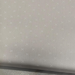 May include: A folded piece of light gray fabric featuring a repeating pattern of small, white, cross-shaped symbols. The textile has a visible woven texture and a consistent, uniform appearance across the entire surface of the material.