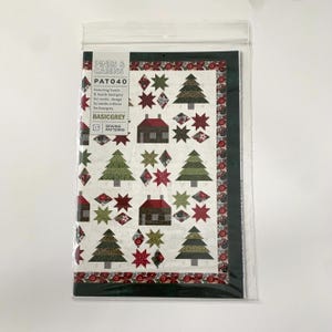 May include: A sewing pattern for a quilt featuring a winter scene with pine trees, houses, and stars. The pattern is called "Pines & Cabins" and is by BasicGrey.