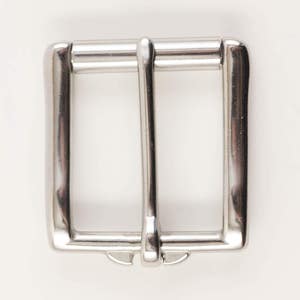 May include: A shiny, silver-colored belt buckle with a rectangular frame and a central bar. The buckle has a classic design, suitable for various belts. The metal has a polished finish, reflecting light.