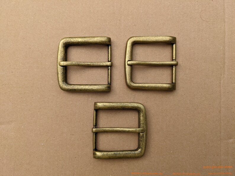 Op de afbeelding: Drie antieke goudkleurige metalen riemgespen. Elke gesp heeft een rechthoekige vorm met een enkele, gecentreerde, horizontale balk.